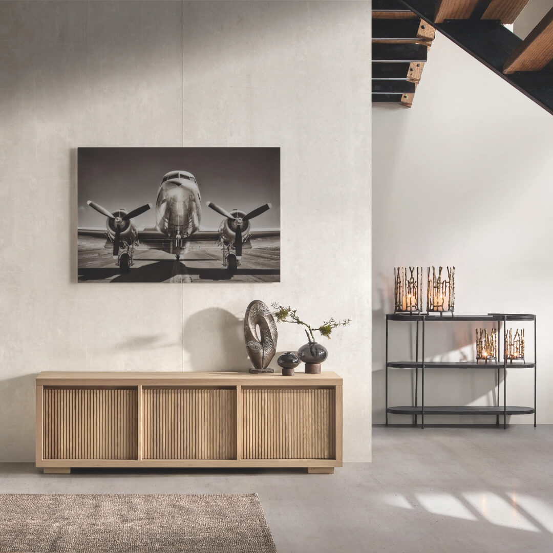 Modern dressoir in lichte kamer met zwart-wit afbeelding van een vliegtuig, naast decoratieve objecten en een rek met kaarsen. Ideaal voor een stijlvol interieur tijdens de 'Cocoon Deals' najaarscampagne.