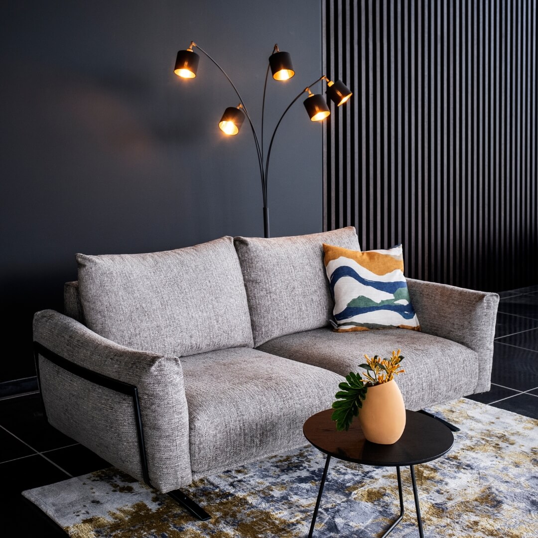 Stijlvolle zithoek met grijze bank en gekleurde kussens, verlicht door een designlamp. Een knusse toevoeging aan het interieur tijdens de 'Cocoon Deals'.