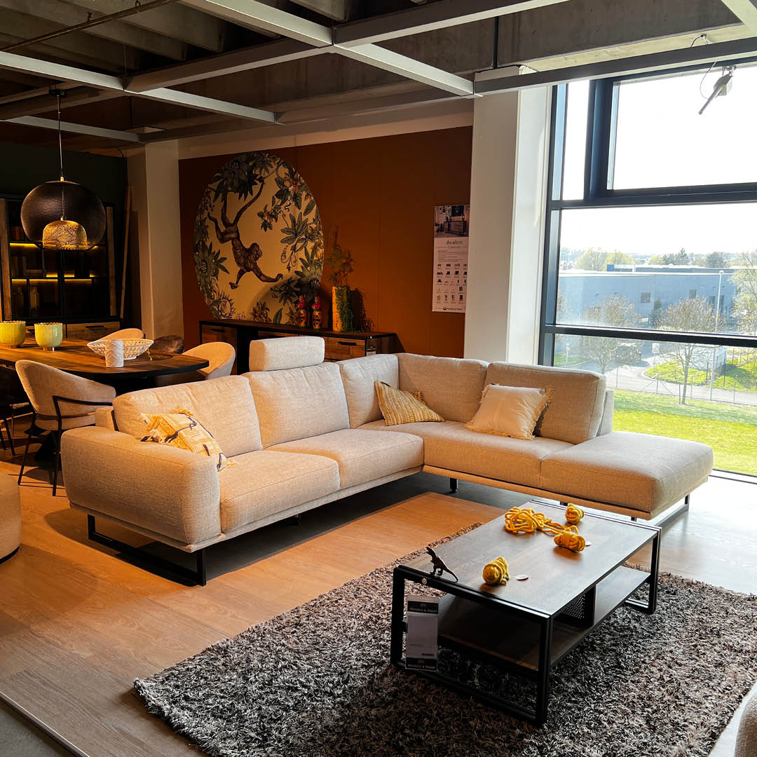 Canapé d’angle en tissu couleur galet clair avec structure en métal noir, présenté avec élégance dans un cadre intérieur chaleureux chez Interieur Avenue Gaverzicht.
